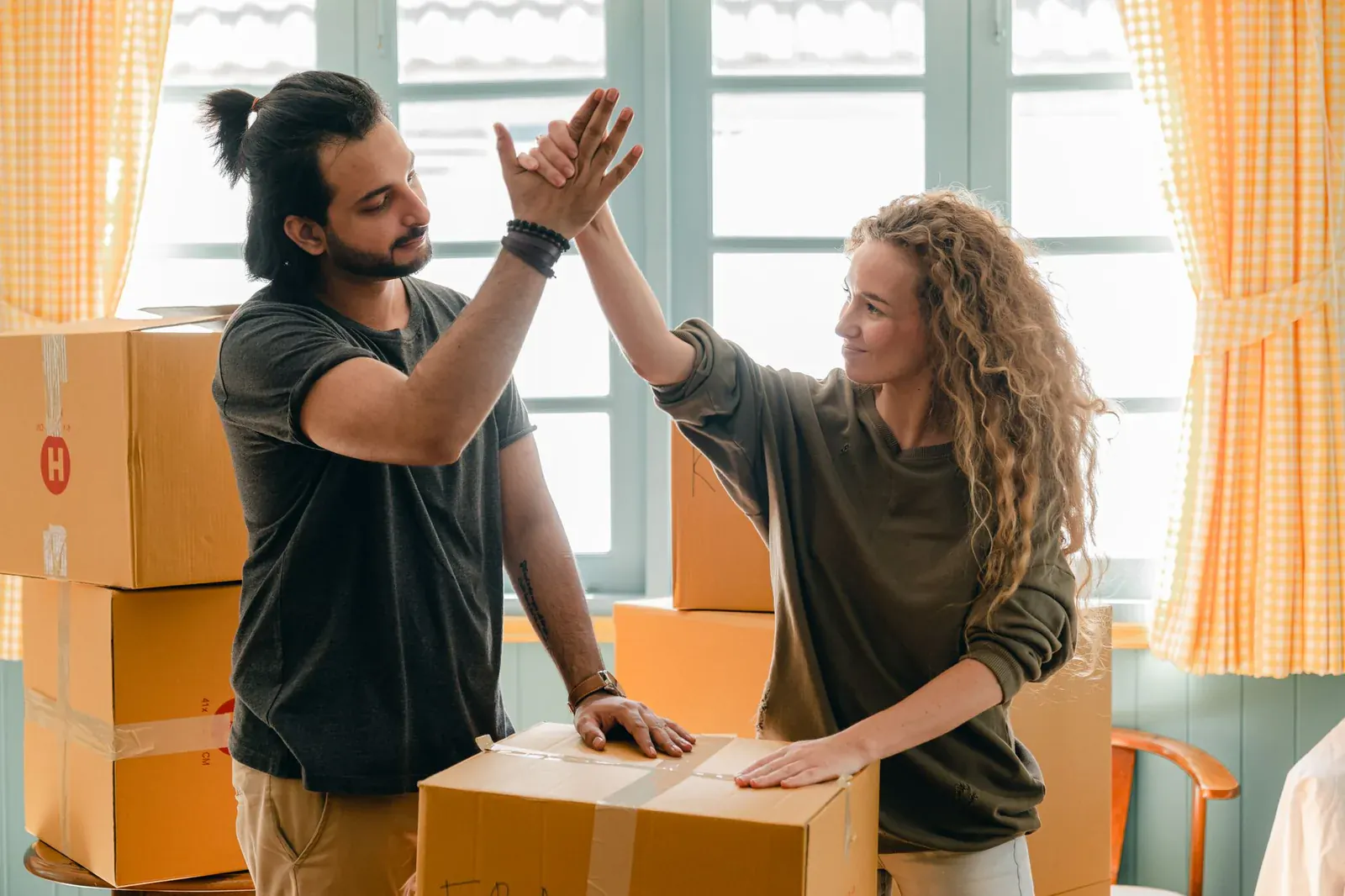 Couple giving a high five beside stacked moving boxes in a sunny room