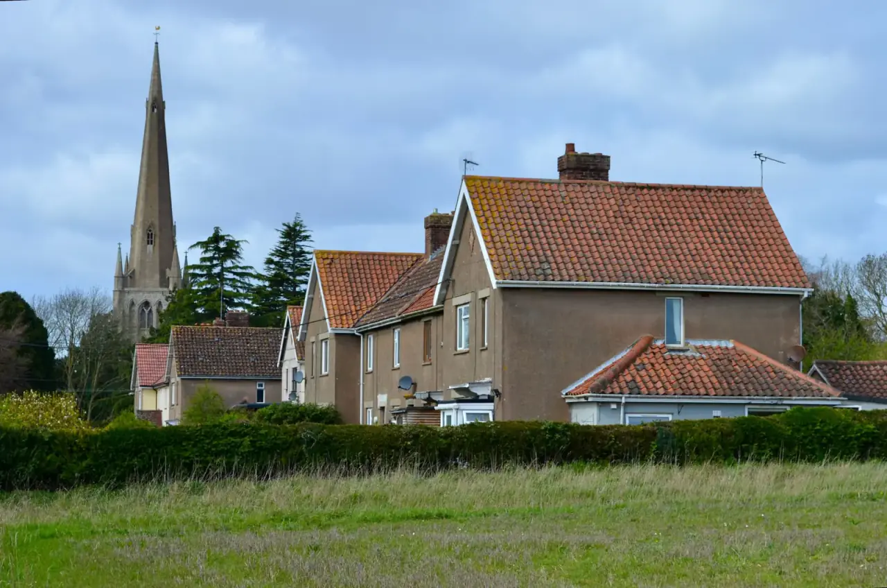 Village church spire rising behind brick houses and a green