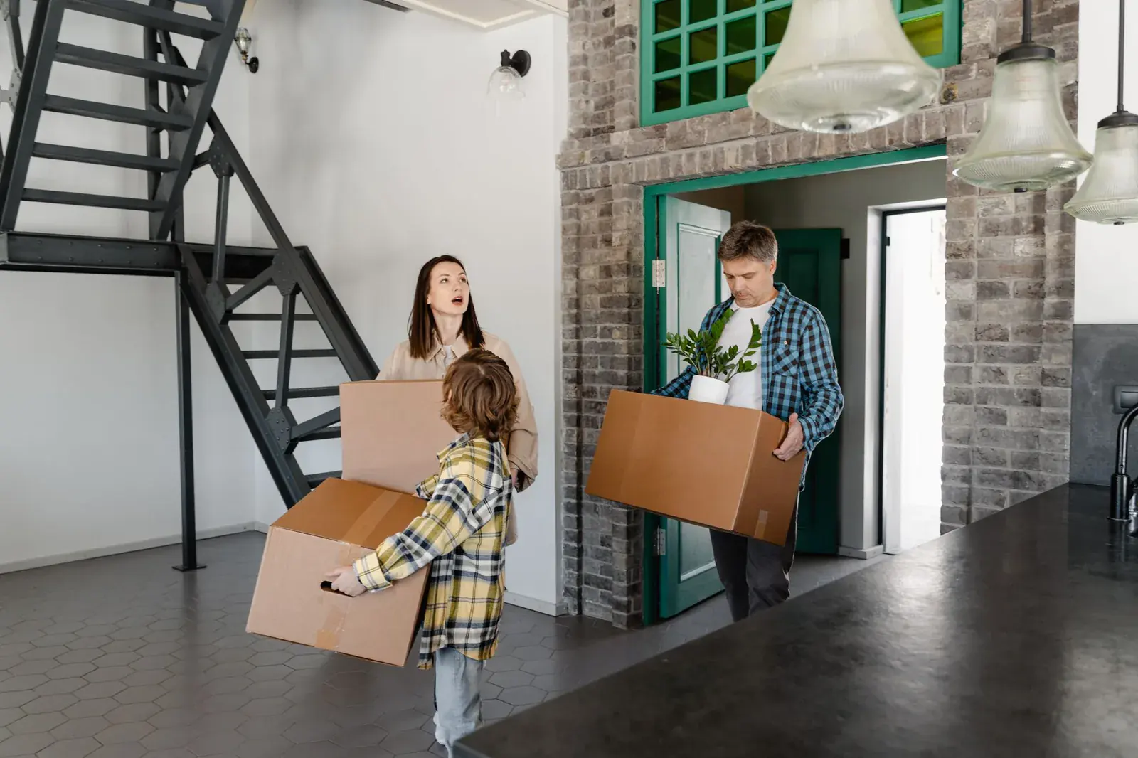 Parents and a child carrying boxes into a new home