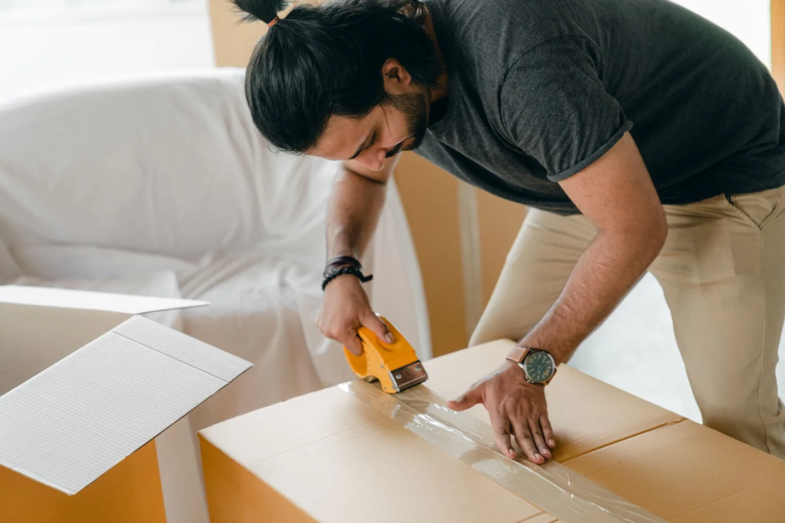 Man sealing a packed cardboard moving box with a tape gun