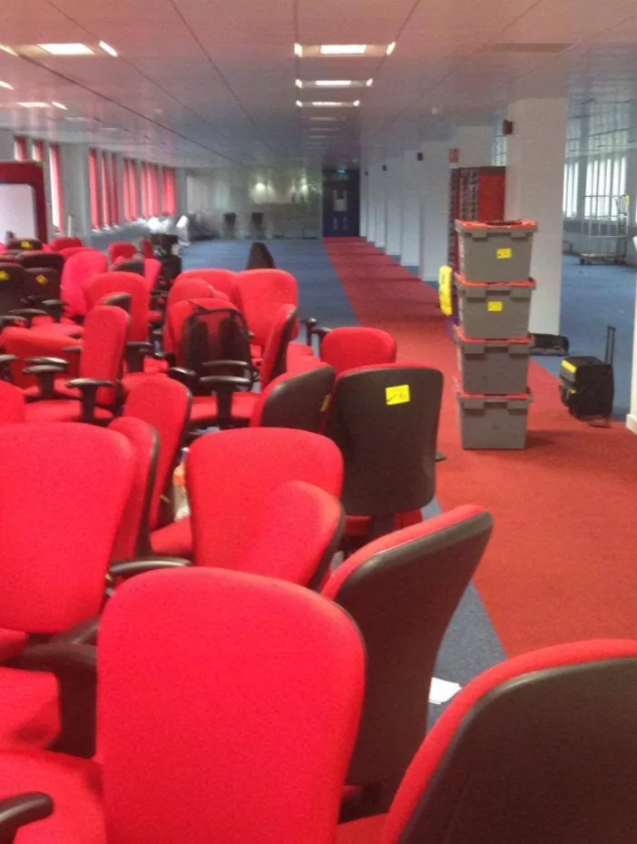 Labelled office chairs and stacked crates lined up in a corridor before an office clearance