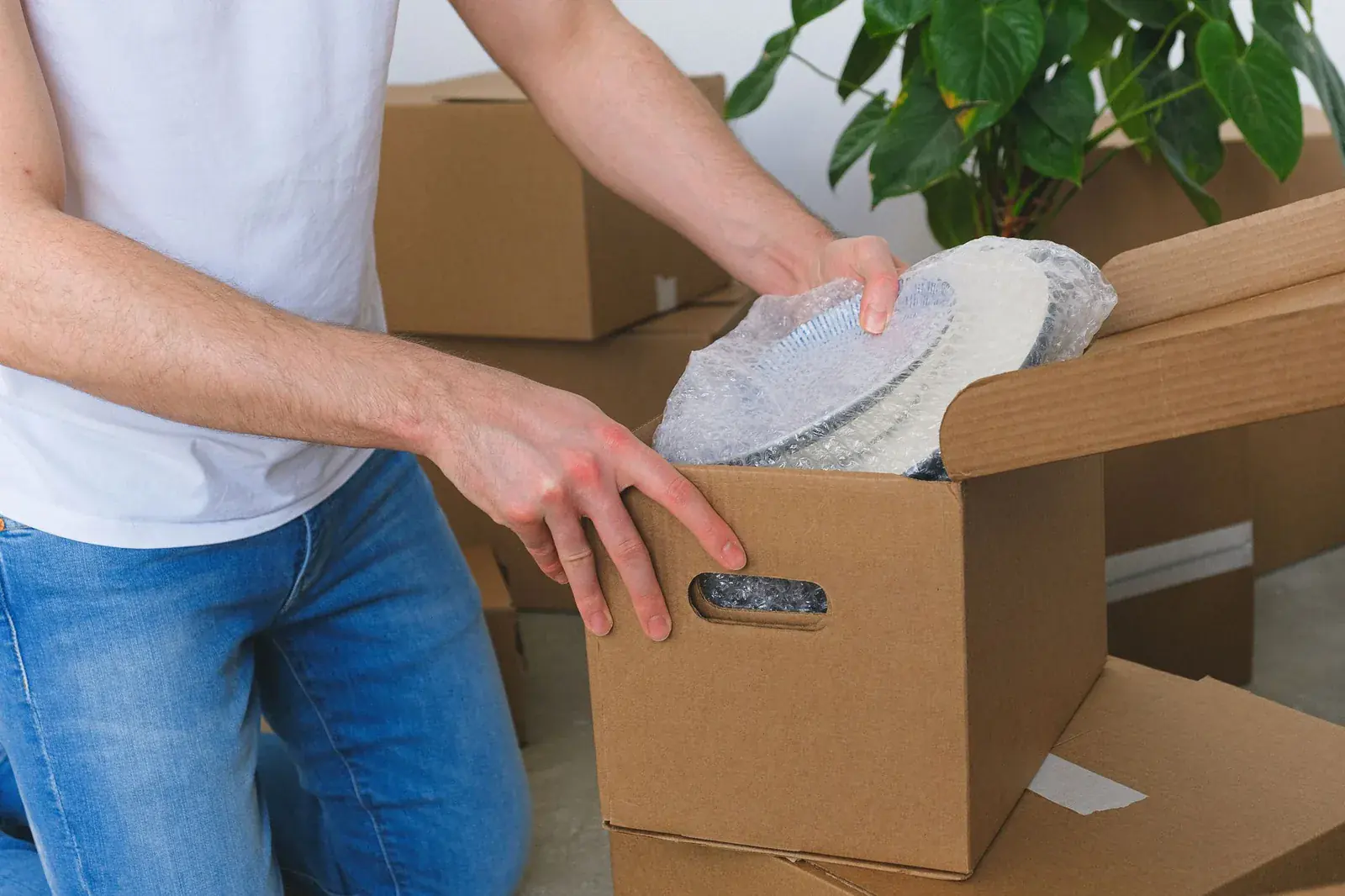 Man packing paper-wrapped dishes into a cardboard box